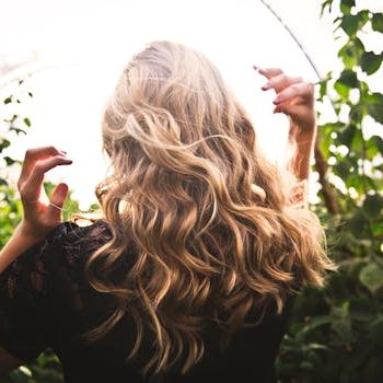 Blonde woman with curly hair surrounded by lush greenery, enjoying a sunny day.