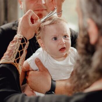 A baby experiencing his first haircut held by his father inside a barber shop.