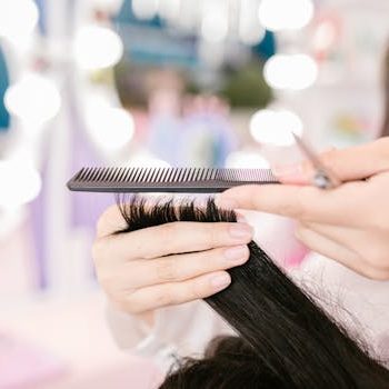 Close-up of a hairdresser grooming hair with scissors and a comb in a salon setting.